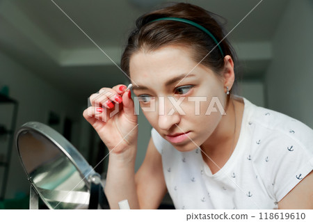 Young girl correcting her makeup in front of the mirror. Home makeup and self-care concept. 118619610