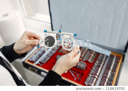Optometrist prepares a set of ophthalmic trial lenses for vision testing and trial frame. Woman open table with optometric instruments. Optometrist wearing white medical coat. 118619702