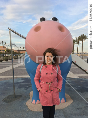Young woman enjoying a delightful playful moment with a charming blue and pink hippo sculpture found in the playground Young woman enjoying a delightful playful moment with a charming blue and pink hippo sculpture found in the playground 118620040