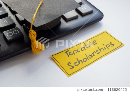 Graduation cap with a note about taxable scholarships. Graduation cap with a note about taxable scholarships. 118620423