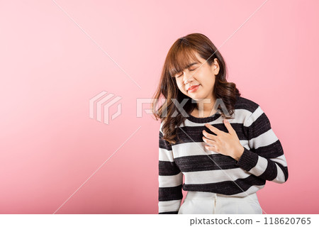 Young woman pressing on chest pain isolated on pink background, painful expression heartache, female having heart attack heart disease, Painful cramps Young woman pressing on chest pain isolated on pink background, painful expression heartache, female having heart attack heart disease, Painful cramps 118620765