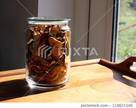 A glass jar with dried apples and fruits stands on a wooden oak table in the sunlight. Diet and healthy eating, vitamins, veganism and vegetarianism. Autumn harvest A glass jar with dried apples and fruits stands on a wooden oak table in the sunlight. Diet and healthy eating, vitamins, veganism and vegetarianism. Autumn harvest 118621106