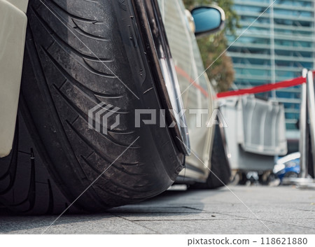 Low profile tire on a modified car parked at a city event showcasing automotive culture during daytime 118621880