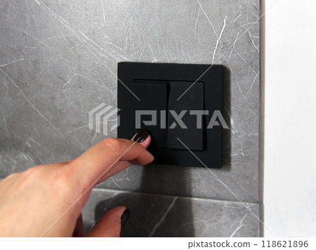 A woman presses the button of a modern black switch against a background of a white wall with gray granite. Technologies and electrics in the interior of the room A woman presses the button of a modern black switch against a background of a white wall with gray granite. Technologies and electrics in the interior of the room 118621896