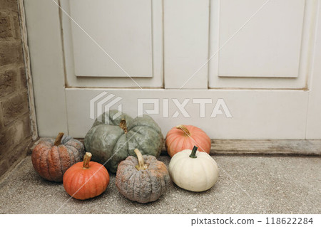Collection of orange, white, green pumpkins. Autumnal decorative display on doorstep. Blurred wooden white front doors background, porch. Halloween, Thanksgiving holiday, fall home decor 118622284