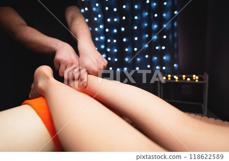 Close-up of male hands giving massage to female legs, spa salon Close-up of male hands giving massage to female legs, spa salon 118622589