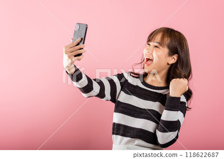 Happy Asian portrait beautiful cute young woman teen smiling excited using mobile phone say yes Studio shot isolated on pink background, Thai female surprised make winner gesture on smartphone Happy Asian portrait beautiful cute young woman teen smiling excited using mobile phone say yes Studio shot isolated on pink background, Thai female surprised make winner gesture on smartphone 118622687