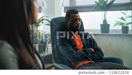 Dolly shot of tired African American man talking to his Asian girlfriend during couples therapy Dolly shot of tired African American man talking to his Asian girlfriend during couples therapy 118622838