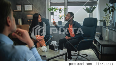 Aggressive African American man yells at his Asian girlfriend during counseling session Aggressive African American man yells at his Asian girlfriend during counseling session 118622844