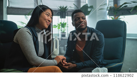 Happy multiethnic couple sit on chairs holding hands after quarrel on couples therapy Happy multiethnic couple sit on chairs holding hands after quarrel on couples therapy 118622902