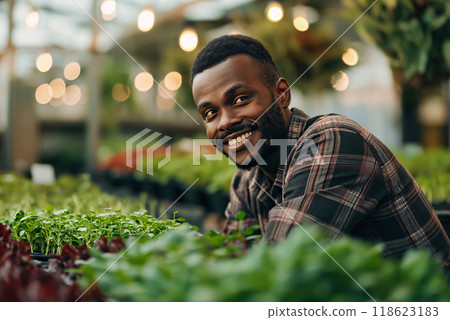 Smiling male farmer tending plants in lush greenhouse environment 118623183