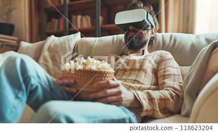 Man on couch with VR headset and popcorn immersed in virtual experience. Leisure tech activities 118623204