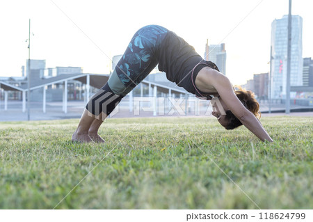 Woman doing downward dog yoga pose in a city park... 118624799