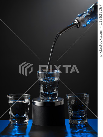 Vodka pouring from the bottle into a glass on a dark background. Vodka pouring from the bottle into a glass on a dark background. 118625267