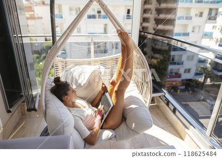 A Relaxing Woman Enjoying Reading a Book While Lounging in a Cozy Hammock on a Balcony 118625484