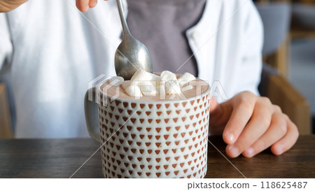 Close-up of a young girl enjoying marshmallows from her hot cacao in a cozy cafe on a chilly winter day 118625487