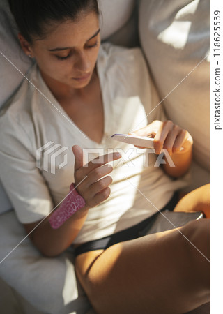 A Relaxed Young Woman Engaged with Her Smartphone While Sitting Comfortably on a Sofa A Relaxed Young Woman Engaged with Her Smartphone While Sitting Comfortably on a Sofa 118625539