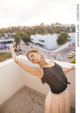 A Graceful Dance Pose on a Balcony at Sunset, showcasing the elegance of movement and beauty A Graceful Dance Pose on a Balcony at Sunset, showcasing the elegance of movement and beauty 118625604
