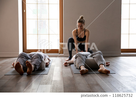 Young slim female yoga instructor leads meditation and stretching class small group people in room 118625732