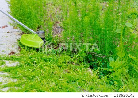 Worker mows green grass on lawn with hand trimmer during lawn care weed management Worker mows green grass on lawn with hand trimmer during lawn care weed management 118626142