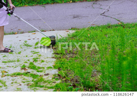 Grass is mowed by worker using hand trimmer in during lawn care weed garden. 118626147