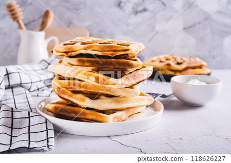 Stack of freshly baked Belgian waffles on plate and sour cream in bowl on table Stack of freshly baked Belgian waffles on plate and sour cream in bowl on table 118626227