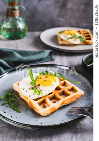 Belgian waffle with fried egg, arugula and spices on a plate on the table vertical view 118626238