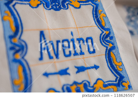 Detailed embroidery on white fabric featuring the word Aveiro in blue thread, framed by an intricate blue and yellow border. Traditional craftsmanship from Aveiro, Portugal. 118626507