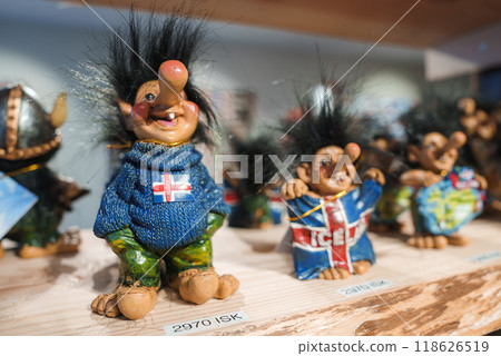 A collection of unique Icelandic troll figurines displayed on a wooden shelf. The trolls feature exaggerated noses, wild black hair, and colorful clothing, including one with an Icelandic flag sweater A collection of unique Icelandic troll figurines displayed on a wooden shelf. The trolls feature exaggerated noses, wild black hair, and colorful clothing, including one with an Icelandic flag sweater 118626519