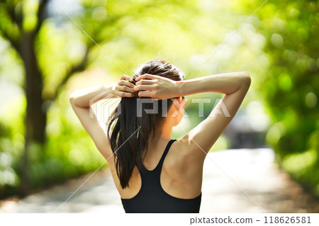 Rear view of a young woman in sportswear running in the greenery 118626581
