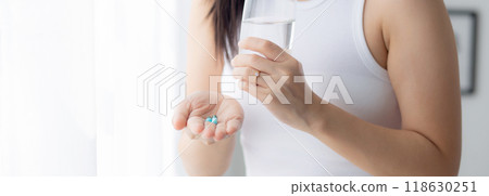Young asian woman holding drug and glass of water while ill standing in the bedroom at home. 118630251