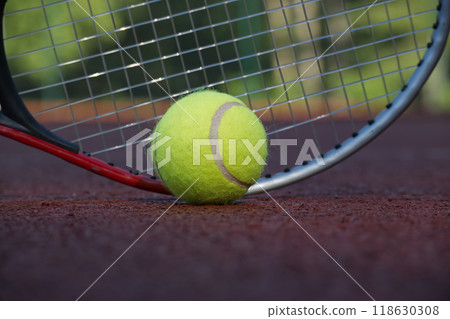 Close-up of tennis ball and racket against net on clay court Close-up of tennis ball and racket against net on clay court 118630308