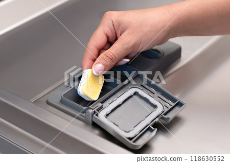 female hand puts dishwasher tablet into open automatic built-in dishwasher machine. Close up female hand puts dishwasher tablet into open automatic built-in dishwasher machine. Close up 118630552