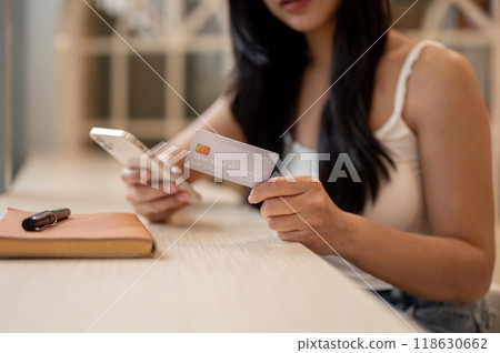 A close-up of a beautiful Asian woman holding her credit card and a smartphone, paying bills online. A close-up of a beautiful Asian woman holding her credit card and a smartphone, paying bills online. 118630662