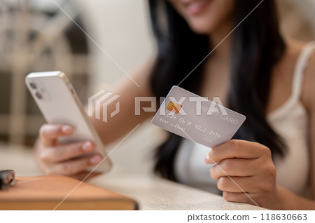 A close-up of a beautiful Asian woman holding her credit card and a smartphone, paying bills online. 118630663
