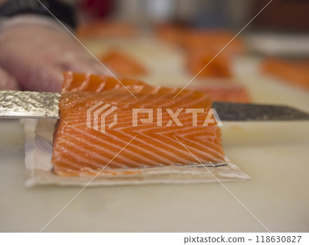 A master chef skillfully cuts fresh salmon into uniform pieces The gloved hands ensure precision as the knife glides through the salmon, showcasing its vibrant color and tender texture. A master chef skillfully cuts fresh salmon into uniform pieces The gloved hands ensure precision as the knife glides through the salmon, showcasing its vibrant color and tender texture. 118630827