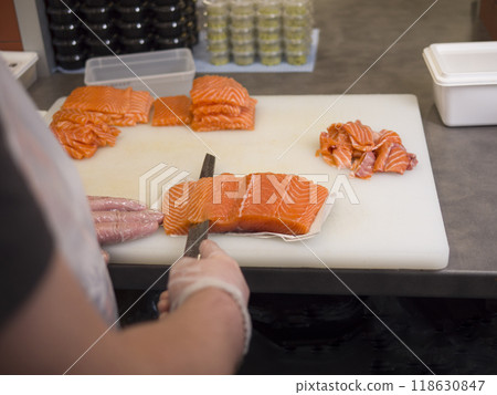 The chefs gloved hands move gracefully as he cuts fresh salmon into even pieces His special knife glides through the salmon, ensuring that each slice of salmon is perfectly even. The chefs gloved hands move gracefully as he cuts fresh salmon into even pieces His special knife glides through the salmon, ensuring that each slice of salmon is perfectly even. 118630847