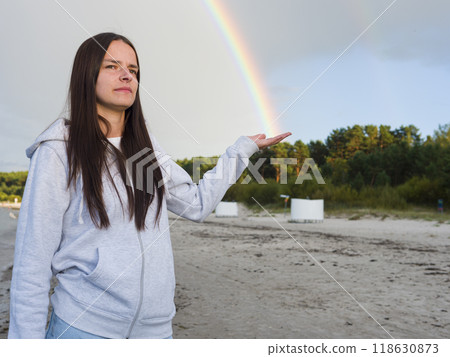 On the beach, Woman Young Brunette reaches out, catching a Rainbow in her hand. The delicate hues of the Rainbow dance against backdrop of waves, as she gazes at Rainbow's shimmering light. On the beach, Woman Young Brunette reaches out, catching a Rainbow in her hand. The delicate hues of the Rainbow dance against backdrop of waves, as she gazes at Rainbow's shimmering light. 118630873
