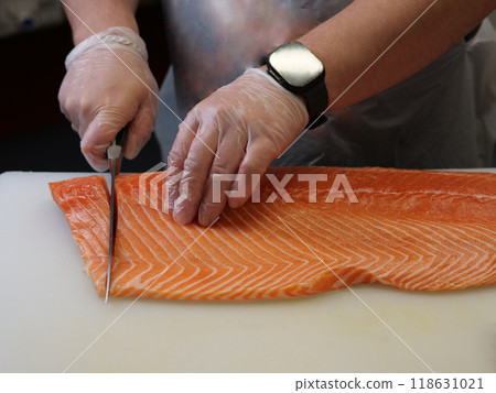 A beautiful large salmon is carefully cut into even pieces with sharp knife on kitchen board Each slice reveals the delicate texture of the salmon, showcasing its natural freshness and vibrant color. A beautiful large salmon is carefully cut into even pieces with sharp knife on kitchen board Each slice reveals the delicate texture of the salmon, showcasing its natural freshness and vibrant color. 118631021