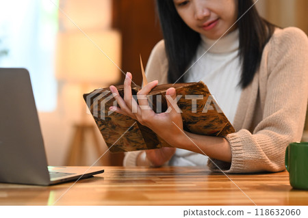 Calm young woman sitting at kitchen table with laptop and reading book 118632060