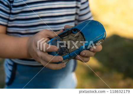 A child holds a toy car in his hand, filling it with sand. A toy in the hands 118632179