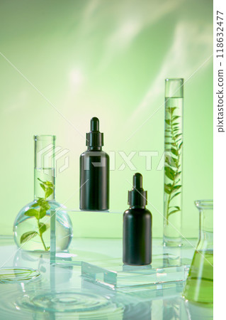 Two black serum droppers sit on a clear acrylic pedestal, surrounded by liquid containers and fresh plants. The light blue backdrop is perfect for beauty product advertising. Two black serum droppers sit on a clear acrylic pedestal, surrounded by liquid containers and fresh plants. The light blue backdrop is perfect for beauty product advertising. 118632477