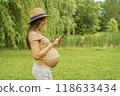 Pregnant woman om phone app reading about pregnancy or shopping baby clothing online. Portrait of happy smiling expectant mother in 3rd trimester in city park nature. Asian girl showing tummy belly 118633434