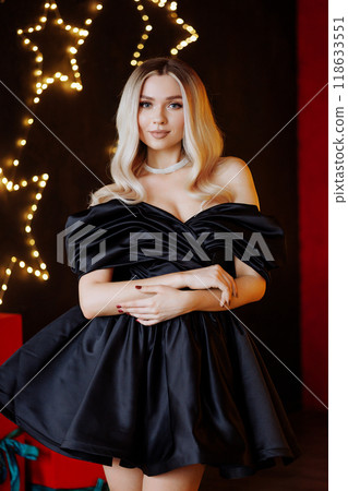 Blonde woman in black dress posing for photo in front of Christmas tree 118633551
