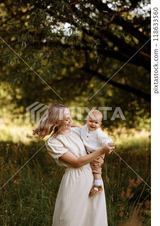 Happy woman holding a small child in her arms in the summer in a park Happy woman holding a small child in her arms in the summer in a park 118633560