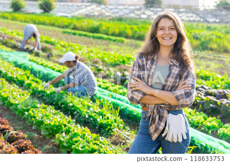 Positive woman owner of plantation garden is resting standing after work and tasks Positive woman owner of plantation garden is resting standing after work and tasks 118633753