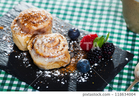Tasty cinnamon rolls with fresh berries and powdered sugar at plate 118634004