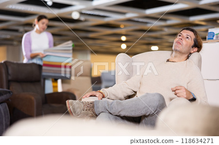 Man looking for armchair in furniture showroom Man looking for armchair in furniture showroom 118634271