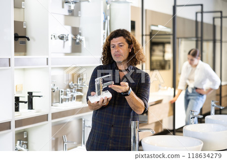 man in plumbing department carefully examines stainless steel water mixer faucet 118634279