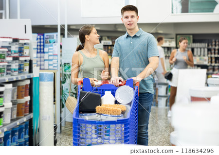 Spouses shopper stand with trolley filled with paint goods for repair and coloring in store sales hall. 118634296